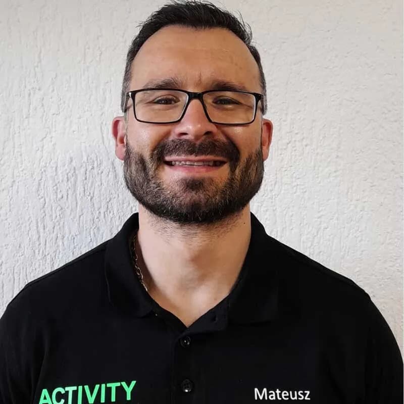 Mateusz, Trainer in Bürstadt, im schwarzen ACTIVITY-Shirt vor heller Wand
