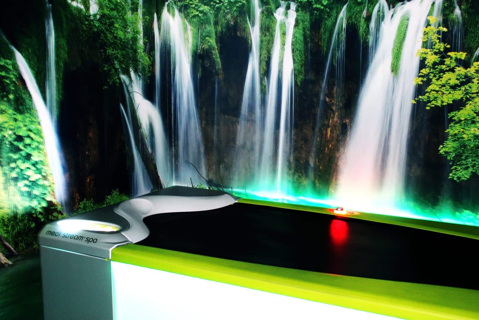 Wasserstrahl-Massageliege mit grünem Rand vor einer Fototapete mit Wasserfall